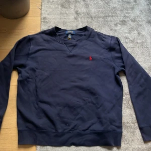 Mörkblå sweatshirt från Polo Ralph Lauren -  Skick 10/10. Storlek 18-20 är som storlek S. Mörkblå sweatshirt från Polo Ralph Lauren med klassisk rund hals och lång ärm. Tröjan har det ikoniska röda broderade polospelar-loggan på bröstet. Tillverkad i mjuk bomull för en skön och avslappnad känsla. Priset kan diskuteras. Säljer på grund av att den inte passar längre