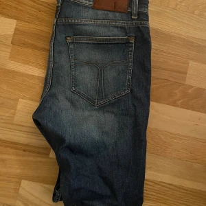 Mörkblå jeans från tiger of sweden - Snygga mörkblå jeans från tiger of sweden med klassisk femficksdesign och slitningar framtill. Jeansen har raka ben och kontrastsömmar, samt en brun läderpatch med T/J-logga bak i midjan. Perfekta för en avslappnad och cool look.