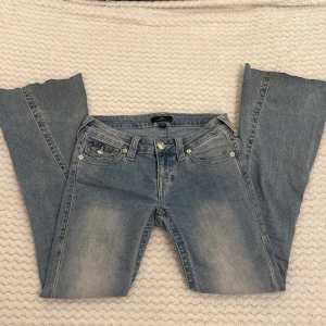 True Religion Joey Low Rise Flare Jeans - Ljusblå jeans från True Religion, modell Joey Low Rise Flare. Klassisk femficksdesign med snygga silverfärgade knappar och detaljerade bakfickor med lock och broderi. Jeansen har låg midja och utsvängda ben för en retro vibe. Tillverkade i mjukt denimtyg. (Jag har oxå klippt dem där nere för att dem va för långa men de va ett tag sen,dom e lite smutsiga men de tvättar ja innan ja postar, såklart)