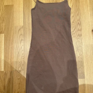 Brun ribbad klänning från Zara - Säljer en brun, ribbad klänning från Zara med smala axelband och figurnära passform. Klänningen är ärmlös och har en enkel, stilren design som gör den lätt att styla. Perfekt för dig som gillar minimalistiska plagg med en modern touch.