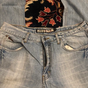 Ljusblå jeans från Blend Denim - Säljer ett par ljusblå jeans från Blend Denim i klassisk femficksmodell. Jeansen är tillverkade i 100% bomull och har snygga slitningar och kontrastsömmar. Regular fit med dragkedjegylf och läderpatch bak i midjan. Perfekta för en avslappnad stil.