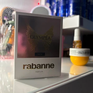 Olympéa Parfum från Rabanne 30ml - Säljer en Olympéa Parfum från Rabanne, 30ml. Flaskan är mörklila och har en rund, elegant form med gulddetaljer och lock. Kommer i en snygg vit och roséguldig kartong med vingar på framsidan. Perfekt för dig som gillar lyxiga dofter och snygg design. Den är helt oanvänd. Bara öppnad förpackningen 