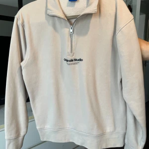 Beige half zip sweatshirt Jack & Jones - Säljer en beige sweatshirt från Originals Studio med half zip och broderad logga på bröstet. Tröjan har hög krage, långa ärmar och är gjord i mjuk bomullsmix.