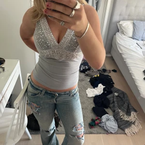 Festtopp - Säljer en snygg silverfärgad linnetopp med djup v-ringning och glittriga paljettdetaljer över bysten. Toppen är tight och ärmlös, perfekt för att sticka ut. Köpt här på Plick!