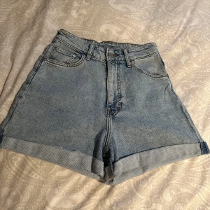 Blå shorts med hög midja från H&M - Säljer ett par ljusblå mom shorts i storlek 34 från H&M i klassisk jeansmodell med hög midja. Shortsen har fem fickor och uppvikta benslut.