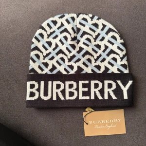Burberry mönstrad stickad mössa - Snygg stickad mössa från Burberry med stort logotryck framtill och ett grafiskt mönster i svart, ljusblått och vitt. Mössan har uppvikt kant och är tillverkad i mjukt stickat material som känns lyxigt och trendigt.
