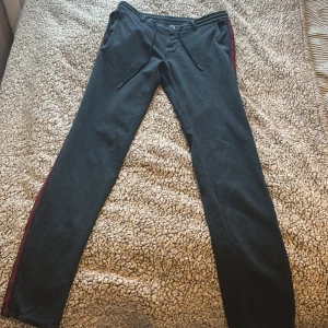 Mörkblå Mason's byxor  - Svarta byxor från Mason's med smal passform och röda ränder längs sidorna. Byxorna har dragsko i midjan, knappgylf och bakfickor med knapp. Perfekta för en sportig och stilren look. Nypris cirka 2000 :-