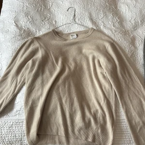 Beige Kashmir från John Henric - Supermjuk beige tröja i 100% kashmir från John Henric. Klassisk rund halsringning, ribbade muddar och snygga förstärkta armbågslappar i en matchande brun nyans. Perfekt för dig som gillar stilrena och lyxiga basplagg.