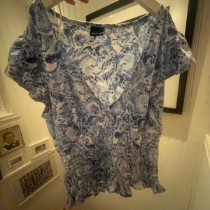 Blommig blå v-ringad blus Gina Tricot - Supersöt blommig blus i blått och vitt från Gina Tricot. V-ringad med korta ärmar, smockad midja och volangkant nertill. Perfekt för dig som gillar romantiska vibes och lätta material.