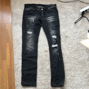 Dsquared jeans - Svarta jeans med skinny fit och coola slitningar på benen samt vita färgstänk för en edgy look. Jeansen har klassisk femficksdesign och dragkedja. Perfekta för dig som gillar streetstyle och vill sticka ut.