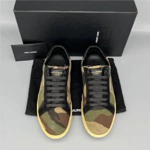 Saint Laurent sneakers i camouflage - Saint Laurent sneakers med camouflage-mönster i grönt, brunt och beige. Skorna har svarta detaljer, snörning och rund tå. Ovandelen är i canvas med svarta mockadetaljer och Saint Laurent-logga på sidan. Sulan är beige och platt för en klassisk streetstil.