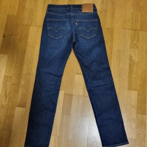 Levi's 511 mörkblå jeans W28 L30 - Snygga Levi's 511 jeans i mörkblå tvätt med klassisk femficksdesign och smal passform. Jeansen har subtila slitningar framtill och är tillverkade i slitstarkt bomullsjeans. Perfekta för dig som gillar en modern och stilren look.