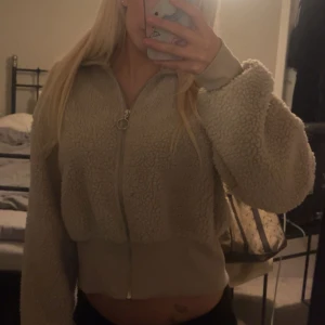 Beige teddyjacka från Bik Bok - Supermjuk och fluffig teddyjacka från Bik Bok i beige färg. Jackan är croppad med dragkedja framtill och har långa ärmar samt ribbade muddar. Perfekt för dig som vill ha en mysig och trendig look.