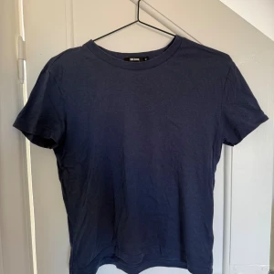 Mörkblå t-shirt från Bik Bok - En enkel och stilren mörkblå t-shirt från Bik Bok i storlek M. Modellen har rund hals och korta ärmar, tillverkad i mjuk bomull som känns skön mot huden. Passformen är normal och t-shirten är helt utan mönster eller detaljer.