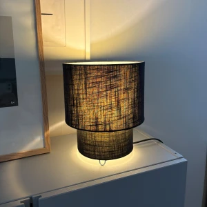 Modern svart bordslampa - Stilren bordslampa med svart tygskärm och cylindrisk form. Ger ett behagligt, varmt ljus och passar perfekt i sovrum eller vardagsrum. Lampan är i mycket gott skick utan synliga defekter eller slitage. Strömkabel medföljer. Köpt på granit🤗