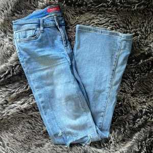 Ljusblå bootcut jeans från Guess - Snygga ljusblå jeans från Guess med bootcut passform och slitna detaljer vid knäna och bensluten. Klassisk femficksmodell med Guess-logga på bakfickan. Jeansen är i mjuk denim och har en riktigt skön vibe.
