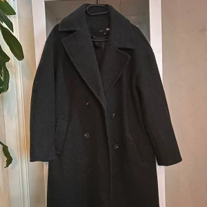Svart ullkappa från 157, XS - Säljer en svart, lång och klassisk kappa från 157 i storlek XS. Kappan har breda slag, dubbelknäppning med svarta knappar och två sidofickor. Materialet är ull och insidan är fodrad för extra värme. Perfekt för höst och vinter. Den är oversized så passar även S.