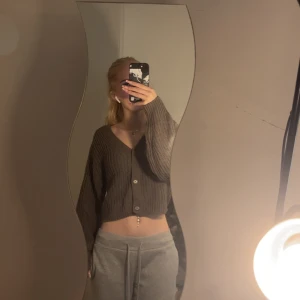 Brun croppad kofta från H&M Divided - Säljer en brun, croppad kofta från H&M Divided i storlek XS. Koftan är stickad med grov ribbad struktur, har v-ringning, 3 stora knappar framtill och långa ärmar. Perfekt för lager-på-lager och chill outfits.