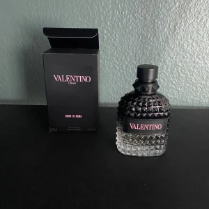 Valentino Uomo Born In Roma EdT 100ml - Säljer en Valentino Uomo Born In Roma Eau de Toilette, 95 ml kvar. Flaskan är i svart och genomskinligt glas med nitar och en lyxig känsla. Märkets logga syns tydligt på både kartong och flaska. Perfekt för dig som gillar exklusiva dofter.