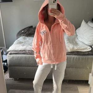 Rosa hoodie från Svea - Rosa hoodie från Svea med dragkedja framtill, broderad logga på bröstet och huva med snörning. Mjuk bomullskänsla och känguruficka. 