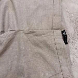 Beige kostymbyxor från Zara - Snygga beige kostymbyxor från Zara i klassisk rak modell. Byxorna har diskreta fickor bak och är tillverkade i ett vävt material som ger en stilren look. Perfekta för dig som gillar en clean och dressad stil.