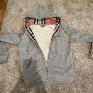 Grå hoodie från Burberry med dragkedja - Säljer en grå hoodie från Burberry i storlek M. Storlek M men passar också S. Jag är 178 och den passar mig perfekt. Den är fin och perfekt till vintern så passa på för en skön o snygg tröja. Pris kan diskuteras litegrann