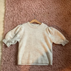 Beige stickad tröja från Gina Tricot - Superfin beige stickad tröja från Gina Tricot med puffiga trekvartsärmar och ribbade muddar. Perfekt för lager-på-lager och ger en trendig look till din outfit. Mjuk och skön, passar till både jeans och kjol.