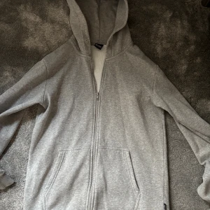 Grå hoodie med dragkedja Only & Sons - Grå hoodie från Only & Sons med hel dragkedja framtill och två stora fickor. Tröjan har huva med snörhål och är tillverkad i mjuk bomullsblandning. Perfekt för chill dagar och enkel att matcha med det mesta. Skicket är 9/10, använd fåtal gånger! 