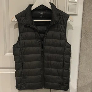 Svart dunväst från Uniqlo XXS - Säljer en svart, ultralätt dunväst från Uniqlo i storlek XXS. Västen är quiltad med horisontella sömmar, har dragkedja framtill och hög krage. Perfekt att packa ner i medföljande påse när du är på språng. Skick 9/10✅