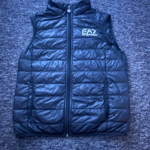 Svart dunväst från EA7 Emporio Armani - Schysst och stilren svart väst från EA7! Är relativt tunn så perfekt att ha över en t-shirt elr hoodie✅