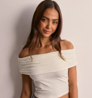  Nelly offshoulder  vit topp - Säljer en snygg offshoulder topp i vit färg. Toppen har en omlottliknande drapering över axlarna. Perfekt att styla med jeans eller kjol för en trendig vibe. I storlek M men funkar också om man har S