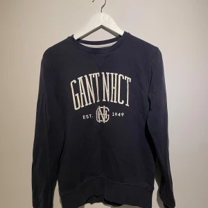 Mörkblå sweatshirt från GANT - Snygg mörkblå sweatshirt från GANT med vit logotyp och tryck framtill. Tröjan har rund hals, långa ärmar och quiltade detaljer på armbågarna. Tillverkad i mjuk bomull som är skön att ha på sig. 