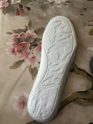 Svarta sneakers från Christian Louboutin - Säljer ett par svarta sneakers från Christian Louboutin med klassisk röd sula och rund tå. Ovandelen är i mjuk mocka med snörning och insidan har en beige skinninnersula. Snygg och stilren design som sticker ut med den ikoniska röda undersidan.