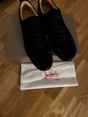 Christian Louboutin svarta sneakers - Svarta sneakers från Christian Louboutin med klassisk röd sula och snörning. . Skorna är tillverkade i mjuk mocka och har rund tå. Kommer med originalkartong och dustbag.