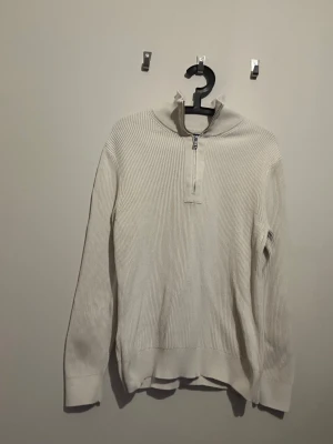 Vit/ Beige ribbad half zip tröja J.Lindeberg - Säljer en stilren vit stickad tröja från J.Lindeberg i storlek S. Tröjan har ribbad struktur, hög krage och half zip-dragkedja framtill. Tillverkad i 100% ekologisk bomull, perfekt för dig som gillar clean och enkel look. Köpt på J.Lindberg för 1500kr. 