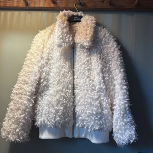 Vit teddyjacka från H&M, storlek 40 - Fluffig och trendig vit teddyjacka från H&M i storlek 40. Jackan har en bred krage, dragkedja framtill och ribbade muddar vid ärmslut och nederkant. Perfekt för dig som vill sticka ut med en mysig och cool look. 🥰