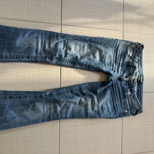 True Religion blå jeans med kontrastsömmar - Snygga blå jeans från True Religion med ikoniska kontrastsömmar och klassisk patch bak. Modellen har fem fickor, knappgylf och cool faded effekt på benen. Perfekt för dig som vill sticka ut med ett street-inspirerat märke. Lite slitna längst ned då jag är förkort!