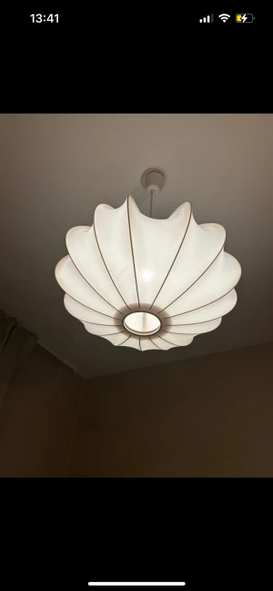 Taklampa i tyg, modern design - Stilren taklampa med vit tygskärm och böljande form, ger ett mjukt och behagligt ljus. Passar perfekt i sovrum eller vardagsrum. Lampan är i mycket gott skick utan synligt slitage eller defekter. Enkel att montera och passar de flesta inredningsstilar.