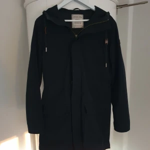 Svart parkajacka från Lexington - Marinblå/svartaktig parkajacka från Lexington med huva och dragkedja framtill. Jackan har två stora fickor och quiltat foder på insidan. Snygg och stilren design med långa ärmar och detaljer i metall på snörningen. Perfekt för kyliga dagar och en "Old money" look. Hör av dig vid minsta lilla fråga