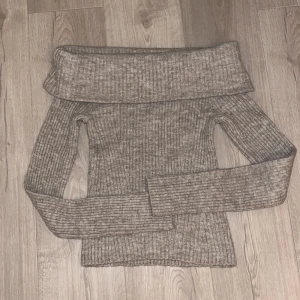 Ribbad offshoulder tröja från H&M - Snygg ribbad stickad tröja från H&M i beige ton. Offshoulder-modell med bred krage som vilar över axlarna. Perfekt för dig som gillar en trendig och chill stil. Materialet är mjukt och stretchigt, vilket gör den skön att bära. Passar dig som vill ha en smickrande siluett.
