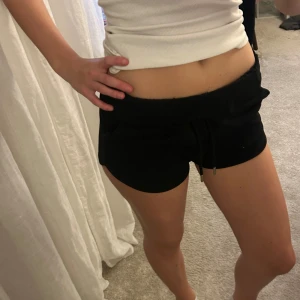 Svarta shorts med snörning - Säljer ett par svarta shorts med låg midja och snörning i midjan. De är korta och har en avslappnad passform, perfekta för chill dagar eller träning. Materialet känns mjukt och bekvämt, troligen bomull eller polyester. Enkla att matcha med allt.