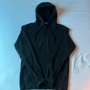 Svart hoodie från The North Face M - Svart hoodie från The North Face i storlek M. Tröjan har broderad logga framtill, huva med snörning och en stor magficka. Tillverkad i 100% bomull för skön känsla. Perfekt för chill dagar och streetwear-stil.