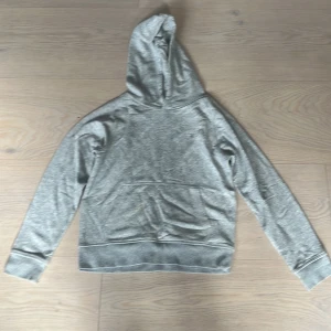  hoodie GANT med broderad logga - Snygg grå hoodie från GANT med broderad logga och sköld på bröstet. Klassisk känguruficka framtill, ribbade muddar och huva. Perfekt för en chill och stilren . 