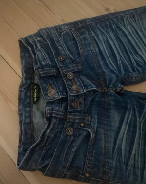 Blå bootcut jeans från Beautiful Jeans Co - Snygga blå jeans med bootcut ben från Beautiful Jeans Co. Jeansen har låg midja och är gjorda i jeansmaterial med kontrastsömmar och broderade bakfickor.