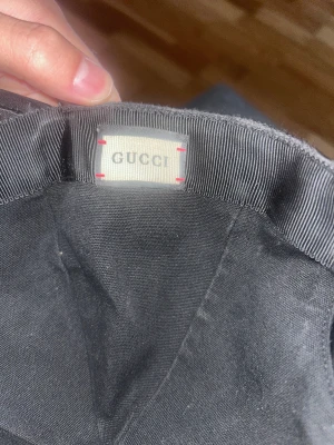 Svart Gucci keps med GG-mönster - Snygg svart keps från Gucci med det klassiska GG-mönstret över hela kepsen. Kepsen har böjd skärm, justerbar rem bak i svart och är tillverkad i slitstark bomull. Perfekt för dig som vill ha en lyxig streetstyle-accessoar.