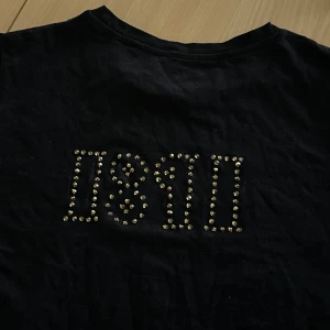 Svart t-shirt 1891  - Svart t-shirt med coolt tryck av siffrorna 1891 på ryggen, dekorerad med glittriga paljetter i guld. Klassisk rund hals och korta ärmar. Tröjan är i grund från lager 157, går att tvätta OBS! Bara i 30 grader, ingen torktumling 