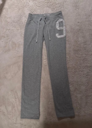 Grå mjukisbyxor med snörning - Snygga grå mjukisbyxor från Abercrombie & Fitch med snörning i midjan och stort tryckt nummer 9 på ena benet. Perfekta för chill dagar eller träning, mjukt bomullsmaterial och normal passform.