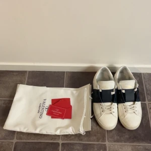Valentino Garavani Open sneakers vit/blå - Snygga Valentino Garavani Open sneakers i vitt skinn med bred blå rem över mitten. Klassisk rund tå, platt sula och diskreta nitar baktill. Kommer med originalpåse och tags. Perfekta för dig som vill ha en lyxig och stilren look.