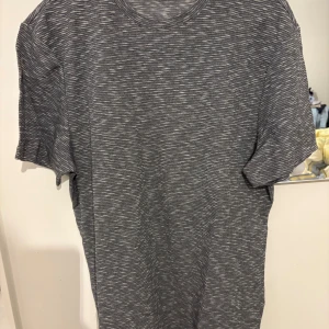 Gråmelerad t-shirt från Primark XL - Säljer en gråmelerad t-shirt från Primark i storlek XL. T-shirten har ett diskret randigt mönster och klassisk rund hals. Materialet känns mjukt och lätt, perfekt för dig som gillar enkel och stilren design.