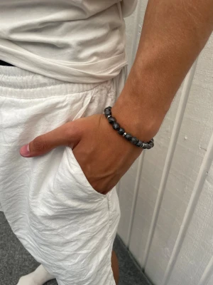 Svart pärlarmband med stendetaljer - Snyggt armband med svarta och gråmelerade pärlor, varvat med små silverfärgade detaljer. Perfekt accessoar för dig som gillar stilrena och coola smycken. Är lätt att matcha med din outfit.
